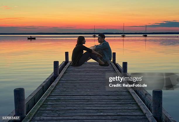 junges paar sitzt auf dem anlegesteg bei sonnenuntergang - romantische stimmung stock-fotos und bilder