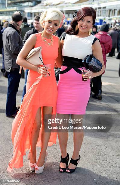 View of two young women wearing dresses in peach and pink, clutch bags and high heeled shoes on Ladies Day during The Grand National Meeting at...