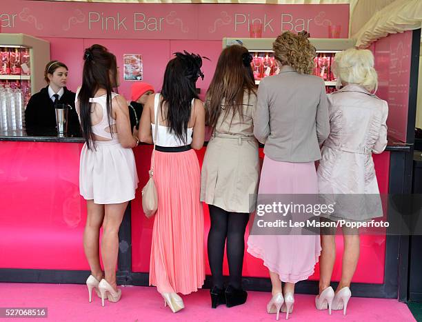 View of five young women wearing a variety of dresses and high heeled shoes as they stand at the Pink Bar to buy drinks on Ladies Day during The...