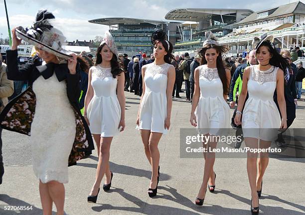 View of four young women wearing matching white dresses and fascinator headwear on Ladies Day during The Grand National Meeting at Aintree racecourse...