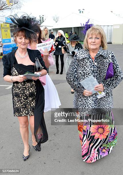 View of two women wearing jackets over dresses with exotic hats and headwear on Ladies Day during The Grand National Meeting at Aintree racecourse...