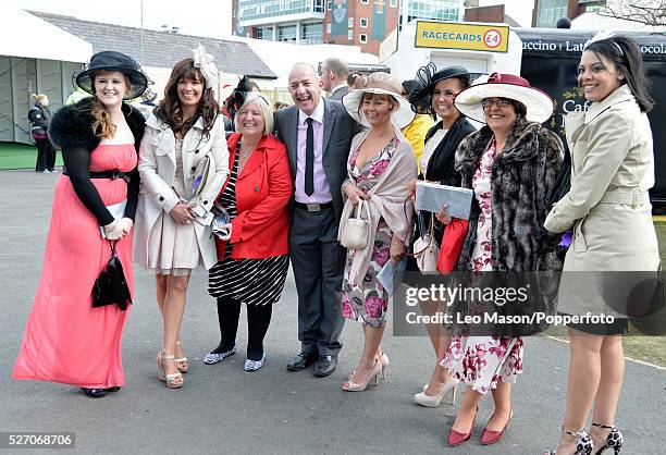 View of a group of seven women, one man and horse racing fans posed together wearing glamorous knee length to full length dresses on Ladies Day...