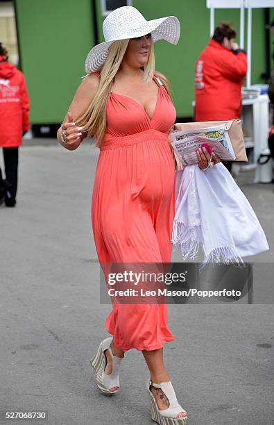 View of a young woman wearing an orange dress, wide brimmed sun hat and high heeled shoes on Ladies Day during The Grand National Meeting at Aintree...