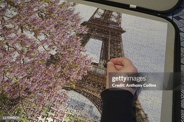 Woman's hand putting final piece into a jigsaw puzzle of the Eiffel Tower in Spring with cherry blossom