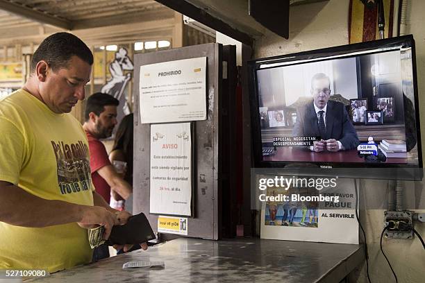 Alejandro Garcia Padilla, governor of Puerto Rico, is seen giving a speech on a television screen as a customer opens his wallet in a bar in San...