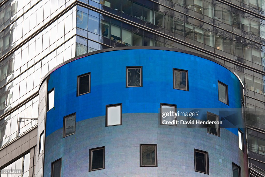 Bright blue and grey cylindrical building in front of a reflective glass skyscraper