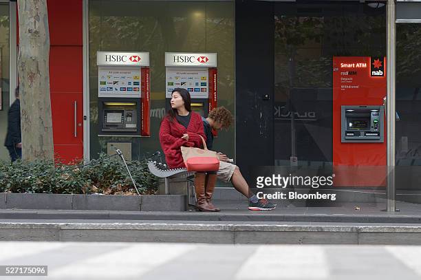 People sit waiting at a tram stop outside a National Australia Bank Ltd. Branch in Melbourne, Australia, on Monday, May 2, 2016. National Australia...