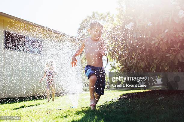 i bambini giocando di irrigazione in erba - annaffiatore foto e immagini stock