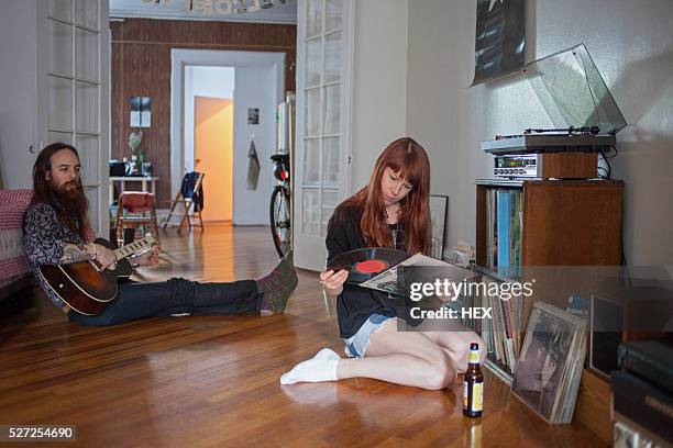 young woman looking at a record album while her boyfriend plays - record player fotografías e imágenes de stock