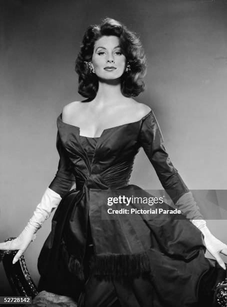 American model and actress Suzy Parker kneels on an Empire chair as she wears a silk gown and long white kid gloves, late 1950s.