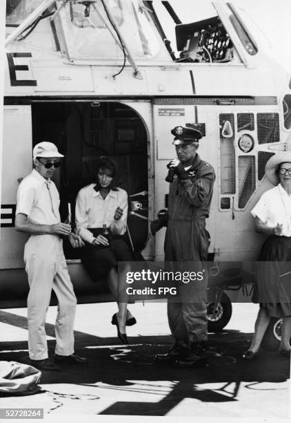 American model and actress Suzy Parker sits in the door of a Sikorsky S-58T helicopter and drinks a coke alongside co-star Richard Widmark and two...