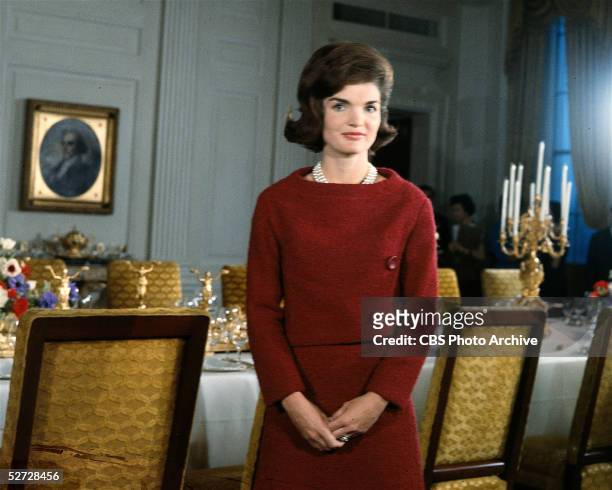 American First Lady Jacqueline Kennedy , in a red dress, stands in before a dining room table in the White House during the filming of a CBS News...