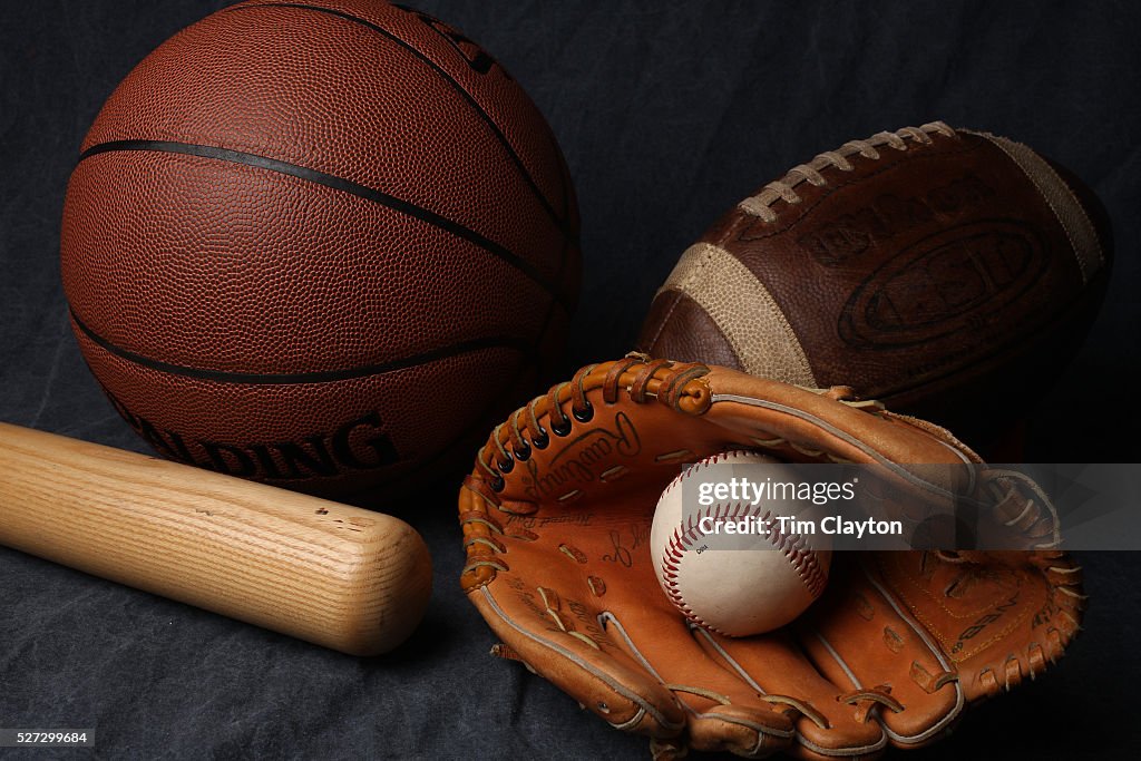 A studio shot of an American Football, a basketball and a baseball ball, mitt and bat.