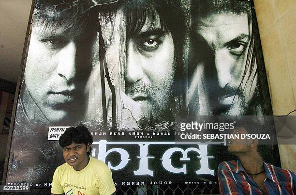 Indian cinema goers sit in front of a billboard advertising the film 'Kaal' outside a cinema hall in south Bombay, 29 April 2005. "Kaal" is the story...