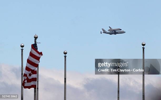 The NASA space shuttle Enterprise, riding on top of a modified jumbo jet, flying at low altitude past an American flag in Liberty State Park, New...