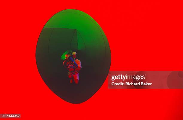 Lone musician kneels to play the tuba within an oval aperture in the art installation sculpture known as Colourscape on Clapham Common, South London,...