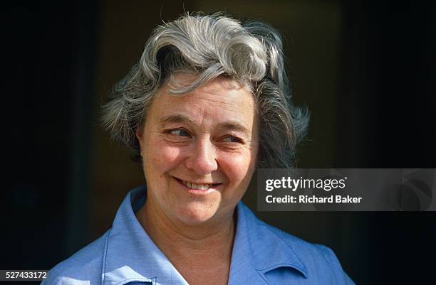 An English caucasian lady smiles at something of interest to the viewer's right. She is a wrinkled female in her sixties, a healthy person with her...