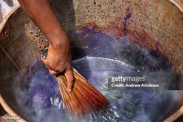 Young girl mixing purple dye with a whisk in a metal bucket to dye material that she sells in a local market, Bamako, Mali.