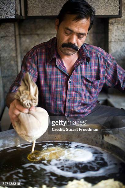 Man squeezes batter from a cloth to make jalebis at the Old and Famous Jalebi Wala . Delhi, India