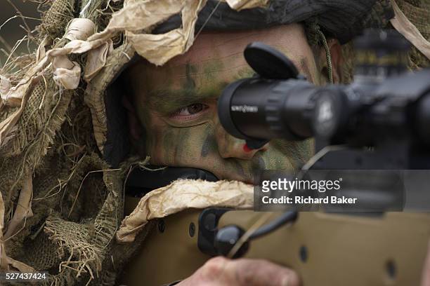 Lying in undergrowth, a camouflaged British infantry soldier is seen looking down the telescopic sight of the new British-made Long Range L115A3...