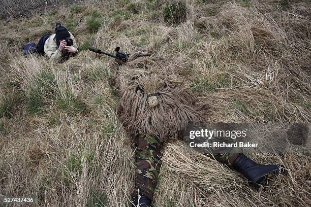 Lying in undergrowth with a photographer shooting pictures, a camouflaged British infantry soldier is seen looking down the telescopic sight of the...