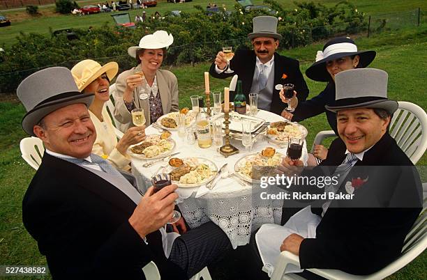 In the middle of a field serving as a grass car park, three couples celebrate the Ladies' Day event at Royal Ascot. Holding their glasses to toast a...