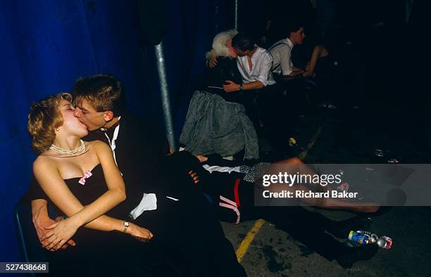 Young adolescent couples kiss and cuddle in a dark corner of a Gatecrashers' Ball in London, England. Three boys and girls dressed in formal...