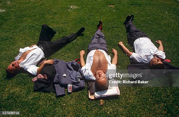 Looking down from above, we see young men who are open-chested and with their suit jackets either beneath their heads or on the grass, three office...