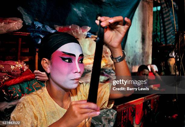 Performer from a Chinese travelling opera wearing traditional makeup and getting ready backstage, Bangkok, Thailand