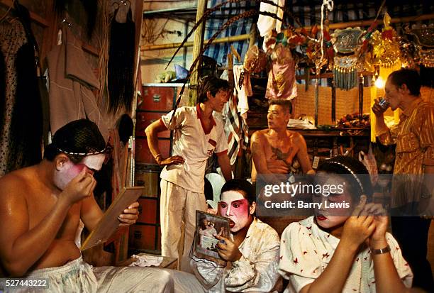 Performers from a Chinese travelling opera putting on traditional makeup and getting ready backstage, Bangkok, Thailand