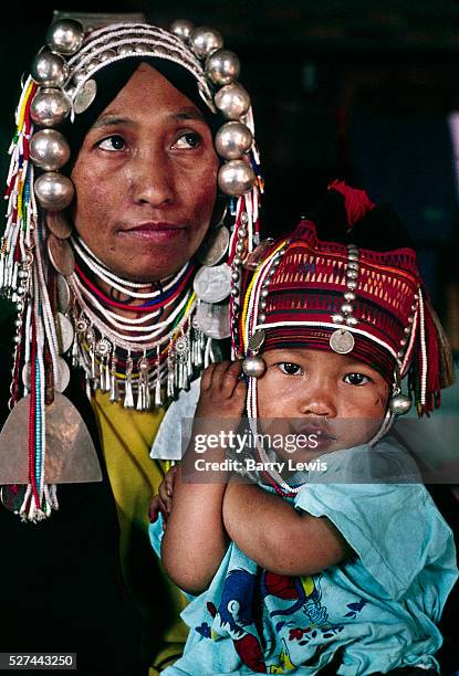 Woman member of the Akha Tribe with her child, wearing an ornate silver headdress and necklaces. The village lies near the Burmese border and the...