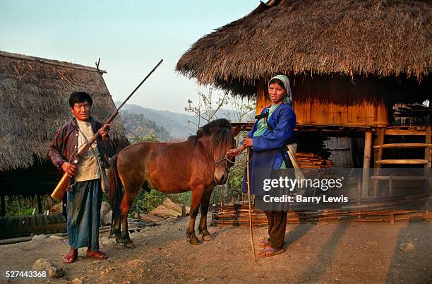 Married couple from the Akha Tribe with their most treasured possessions outside their home: a horse and a shotgun. The village lies near the Burmese...