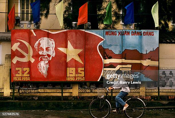 Young boy cycles past a large billboard showing the face of Ho Chi Minh and the Communist hammer and sickle symbol inside the Vietnamese flag in...