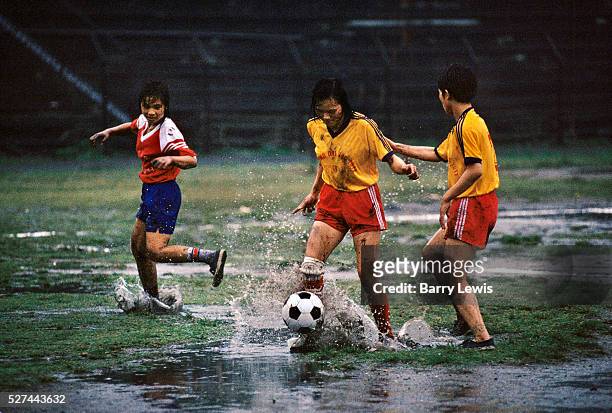 Three young female football players kick a ball around in heavy rain in Cam Pha, northern Vietnam. Their families work in the coal mines nearby.