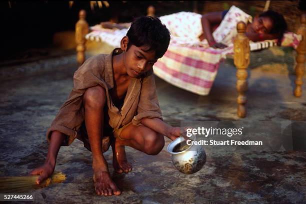 Korlap Rao sweeps the floor whilst his mother, Narayamma lies on a charpoy. She has AIDS and his father has fled. Kasapatanan village, Araku valley,...