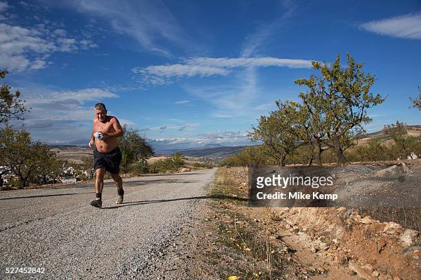 Man out running in the heat through olive groves near to Alhama de Granada, Andalucia, Spain. This is a totally agricultural area, covered mainly...