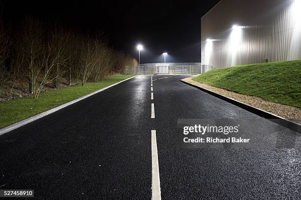 Seen from the middle of the road, an empty highway landscape is seen at night alongside a giant generic warehouse wall at the DIRFT warehouse...