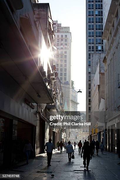 People commutors shadows silhouettes walking in the street between tall buildings in central Sao Paulo, Brazil. Starburst from sun in afternoon light.