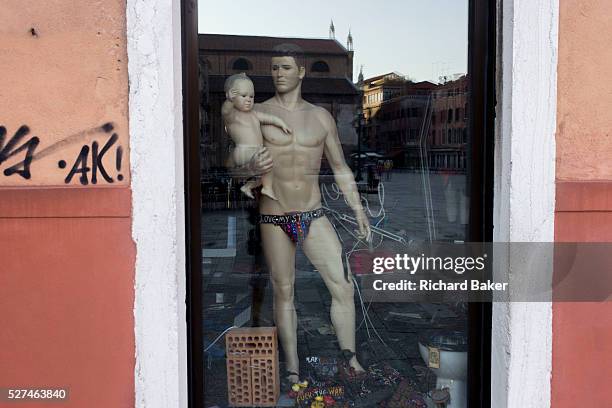 Male mannequin holds a baby in the wondow of a tourist shop in Dorsoduro, a district of Venice, Italy. With a sexy pouch saying 'Love my start-up'...