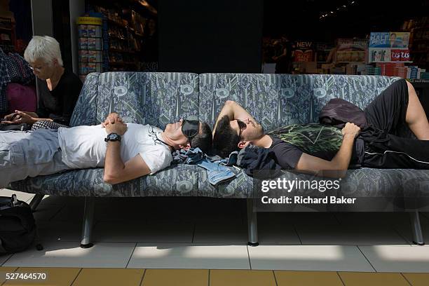 Passengers stretched out on an airport terminal seat at Gatwick, London. Sleeping while waiting for their flight, the two men rest head to head on...