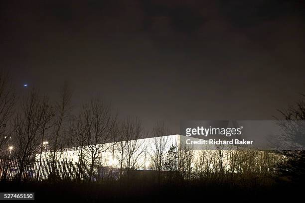 The form of a giant generic warehouse glows from ambient light at the DIRFT warehouse logistics park in Daventry, Northamptonshire England. Bare...