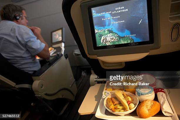 Man tucks in to his in-flight meal on-board an Air France Boeing 777 flight from Paris Orly to Cayenne, French Guiana. Putting more food into his...