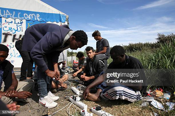 Men charge their cell phones at 'the Jungle' migrant camp in Calais, France, August 10, 2015. The Calais jungle is the nickname given to a series of...