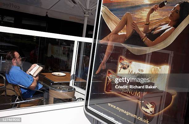 Following UK commercial driving law, a lorry driver relaxes by reading in a window at the M40 motorway services in Warwickshire, England. Leaning...