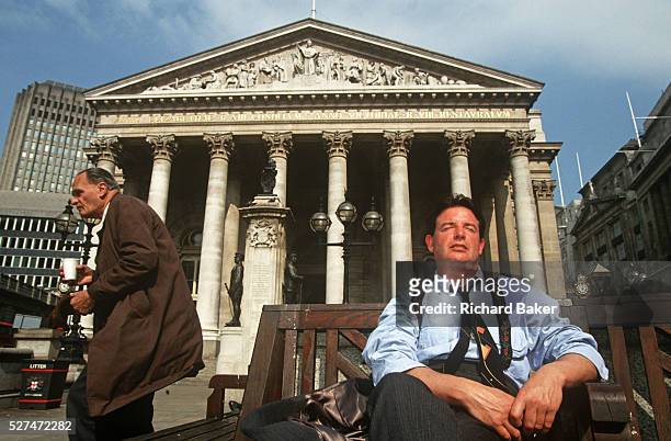 City workers enjoy a lunchtime siesta in summer sunshine under solid Corinthian pillars of the Royal Exchange in City of London. With his tie askew...