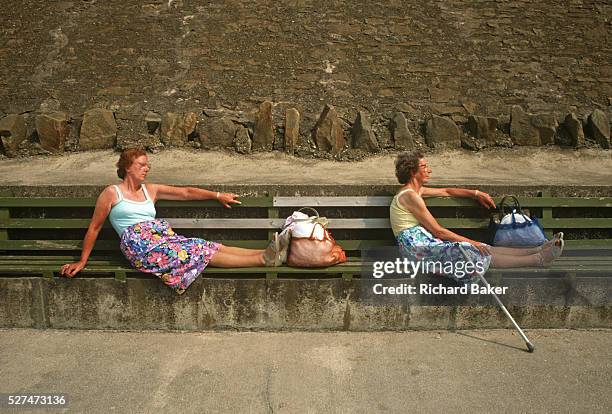 Two sisters sit in identical poses on sea wall benches at Blackpool's Promenade, Lancashire, England. The eccentric pair has adopted the same posture...