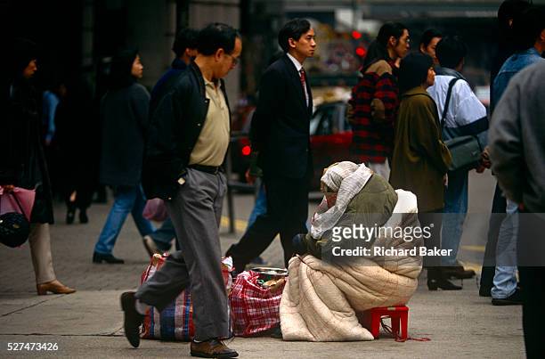 Passers-by ignore a destitute bag lady in a Hong Kong's Tsim Sha Tsui street on the Kowloon side. The poor woman sits amid the bustle and crowds of a...