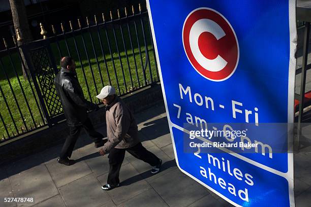 Two pedestrians walk beneath a motorists' Congestion Zone sign on a London street. Seen from the top deck of a bus, we see from an aerial perspective...