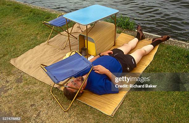 Man rests on a stretch of grass, his face shielded from a bright sky beneath a camping stool during a particularly hot afternoon at the Henley Royal...