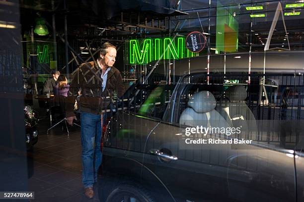 An interested potential buyer looks over a car at a Mini car dealership in London's Park Lane. With sunlight streaming into the otherwise darkened...